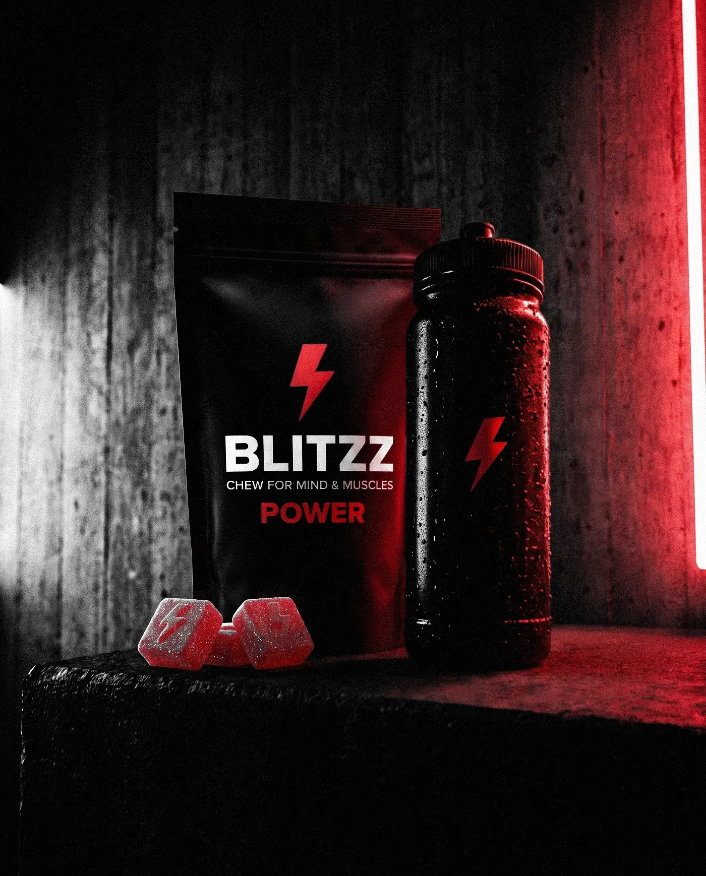 A BLITZZ POWER pack next to a black sports bottle and three red gummies on a concrete ledge